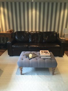 a living room with a black leather couch and ottoman in front of striped wallpaper