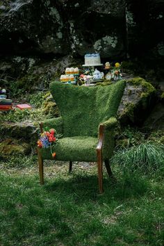 a green chair sitting in the middle of a grass covered field next to a cake and cupcakes