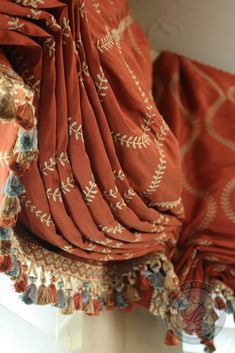 an orange and gold patterned curtain with tassels hanging from it's sides