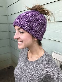 a smiling woman wearing a purple knitted beanie with her hair in the wind