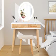 a white vanity table with a mirror and flowers on it in a light colored room