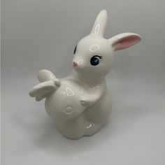 a white ceramic rabbit figurine sitting on top of a gray surface with blue eyes