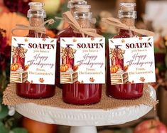 three jars of red liquid sitting on top of a white cake platter with tags