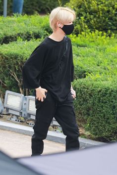 a blonde haired man wearing a black face mask walking down the street with his hands in his pockets