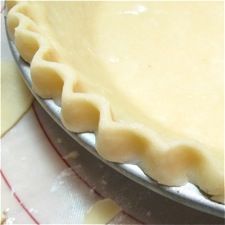 an uncooked pie crust sitting on top of a metal pan next to a red and white checkered table cloth