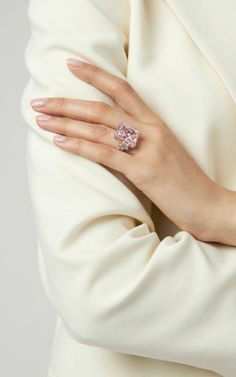 a woman's hand with a pink diamond ring on her left wrist, wearing a white coat