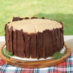 a chocolate cake sitting on top of a wooden platter next to a plaid table cloth