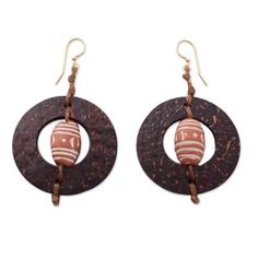 Ornate terracotta beads center coconut shells in the design of these bold earrings. The design of the earrings makes me think of medieval architecture says Nonyem Abena Ibeneme. The earrings are crafted by hand with waxed linen cords and brass hooks. Bohemian Brown Pierced Hoop Earrings, Brown Fair Trade Jewelry For Festivals, Wooden Beads Earrings For Beach, Wooden Beaded Earrings For Beach, Artisan Brown Earrings For Pierced Ears, Fair Trade Brown Jewelry With Round Beads, Brown Fair Trade Round Bead Jewelry, Bohemian Brown Round Earrings, Earthy Brown Earrings For Festivals