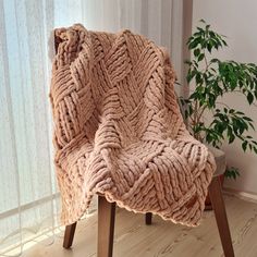 a chair with a blanket on top of it next to a potted green plant