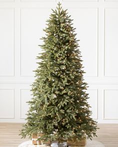 a christmas tree with presents under it on a table in front of a white wall