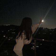 a woman standing on top of a balcony next to a lush green hillside at night