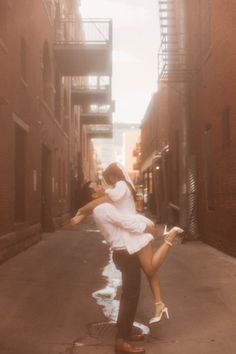 a man and woman are dancing in an alleyway with brick buildings on either side