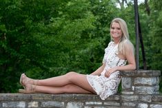 a beautiful woman sitting on top of a brick wall next to a green tree filled forest