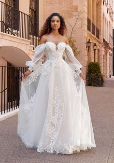 a woman in a white wedding dress standing on the street with her hands on her hips