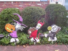 halloween yard decorations in front of a brick building with bushes and shrubbery on the side