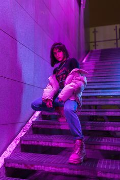 a woman sitting on some steps in front of purple light