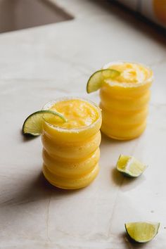 two glasses filled with drinks sitting on top of a counter next to sliced limes