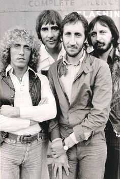 four men standing next to each other in front of a train car with their arms crossed