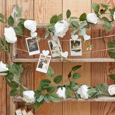 some white flowers and green leaves are hanging from a shelf with pictures on the top