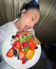 a woman with her mouth wide open over a plate of fruit on a white plate