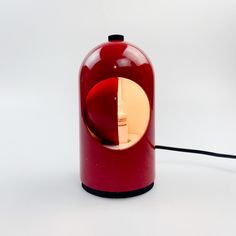 a red table lamp sitting on top of a white floor next to a black cord