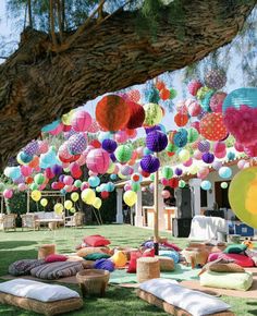 many colorful balloons and pillows are hanging from the trees in front of an outdoor party