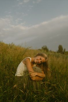 a woman is sitting in the grass with her arms around her chest and looking at the camera