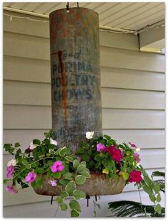 flowers are growing in a hanging planter on the side of a house with an old rusty pole