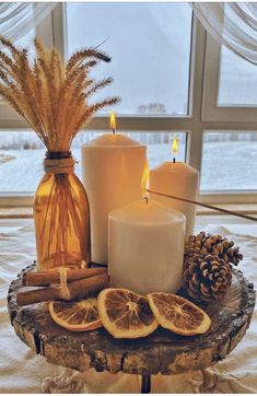 three candles are sitting on a table with orange slices and pine cones in front of them