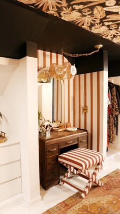 a dressing room with striped wallpaper and an antique bench in front of the mirror