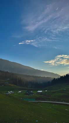 the sun is setting over a green field with mountains in the backgrouds