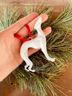 a hand holding a small white dog ornament on top of a pine tree