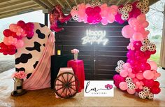 a birthday party with pink and black balloons, cow print decorations, and a wagon