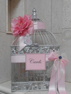 a birdcage with a pink flower in it and a name tag on the front