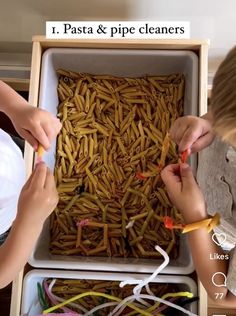 two children are playing with pasta and pipe cleaners in a box that is filled with noodles