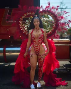 a woman in a red and gold costume standing next to a firetruck with feathers on it