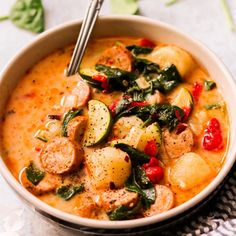 a bowl of soup with sausage, potatoes and spinach on the side next to a spoon