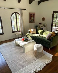 a living room with a green couch and white coffee table in front of two windows