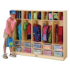 a young boy standing next to a wooden locker with plastic bins and clothes on it