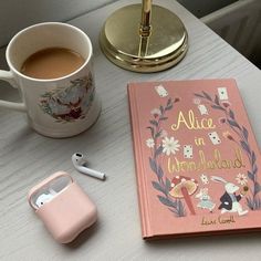 a pink book sitting on top of a white table next to a cup of coffee