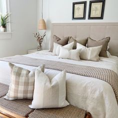 a bed with many pillows on it and two pictures hanging above the headboard,