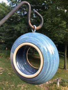 a blue and white ball hanging from a metal hook in a park area with trees behind it