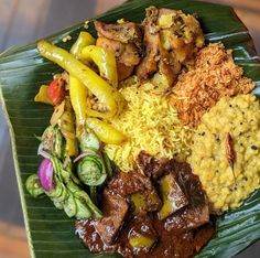 a green plate topped with meat, rice and veggies on a banana leaf