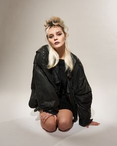 a woman sitting on the ground with her legs crossed and wearing short shorts, black jacket and boots