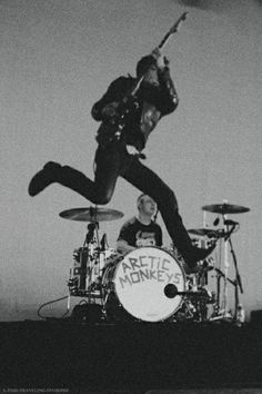 a man jumping up into the air on top of a drum kit while another man plays drums behind him