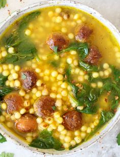 a white bowl filled with soup and meatballs on top of green leafy garnish