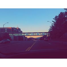 the sun is setting on an empty street with cars driving down it and a bridge in the background