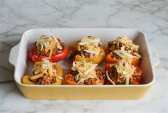 several stuffed peppers in a yellow casserole dish on a marble counter with cheese