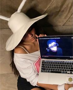 a woman wearing a white hat and holding a laptop computer in front of her face