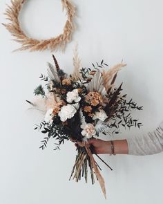 a woman holding a bouquet of flowers in front of a wall hanging on a rope